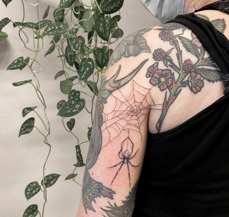 a woman with a spider web tattoo on her arm next to a potted plant