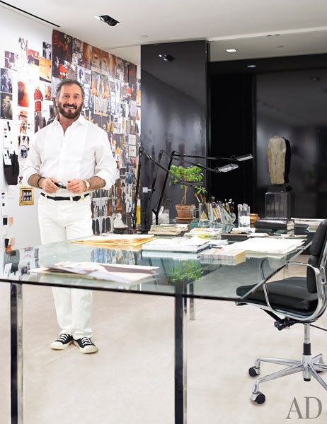 a man standing in front of a glass desk with chairs and pictures on the wall