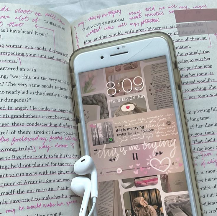 an open book with headphones on it next to a cell phone and earbuds