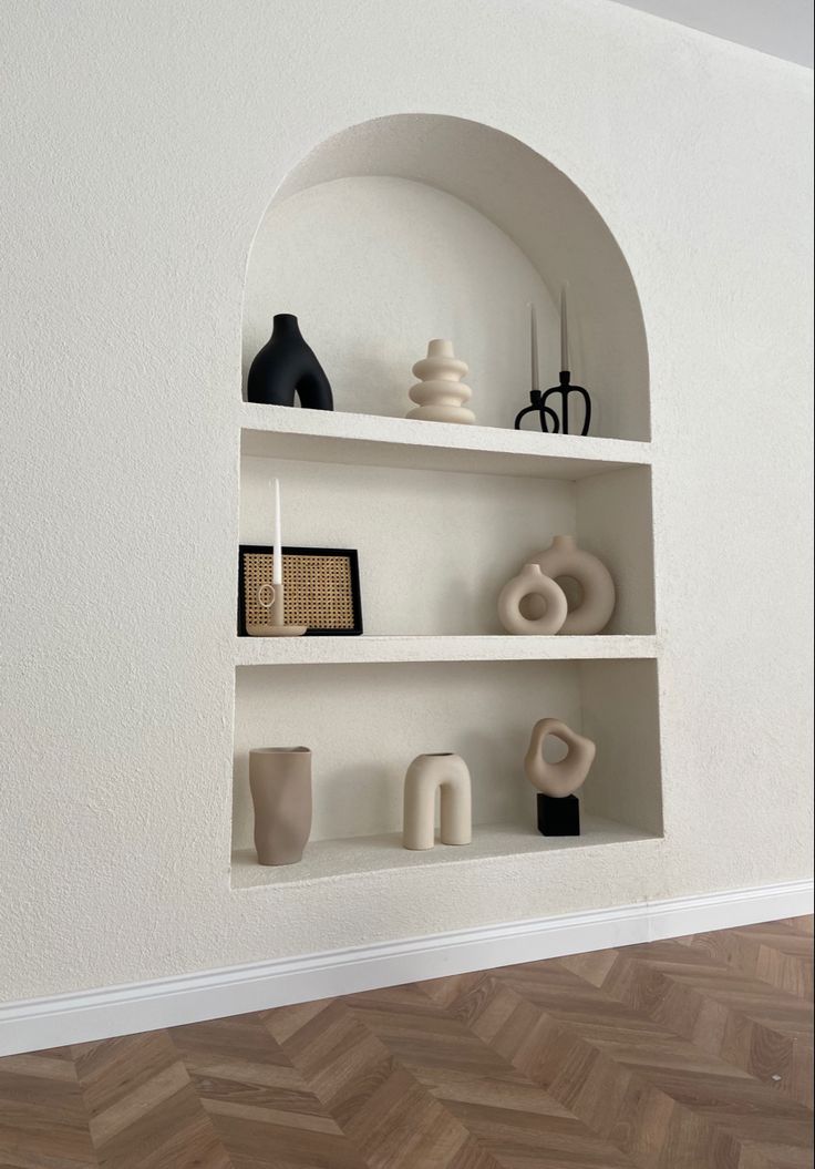 a white shelf filled with vases and other items on top of wooden flooring