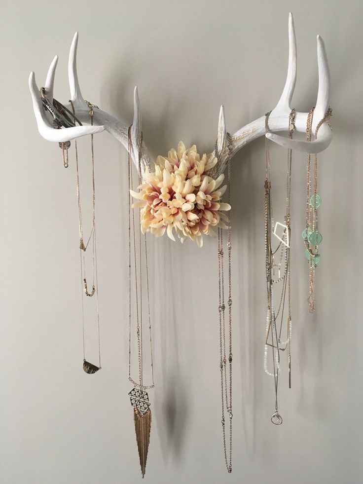 the antler is hanging on the wall with several necklaces and flowers in it