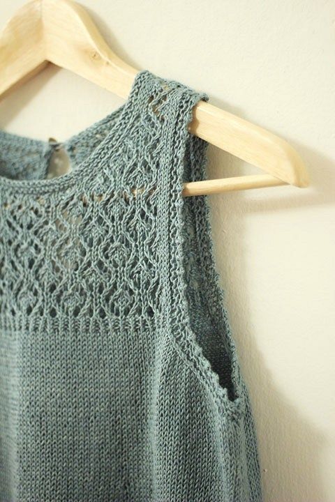 a sweater hanging on a wooden hanger next to a white wall and a blue tank top