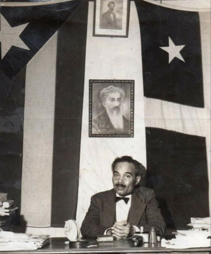 an old black and white photo of a man sitting at a desk in front of flags