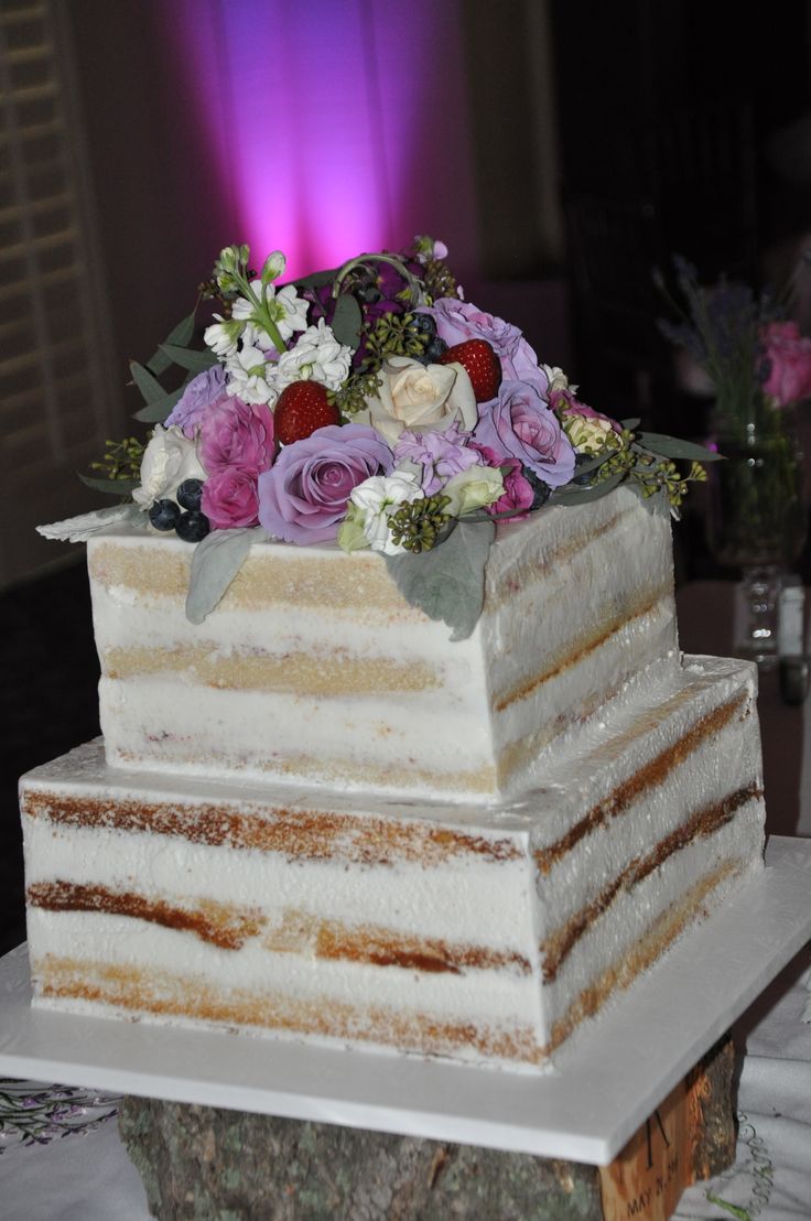 a three layer cake sitting on top of a table with flowers in the middle and purple lights behind it