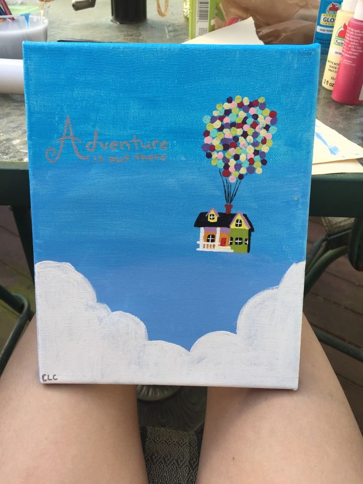 a person holding up a painting with a house and hot air balloon in the sky