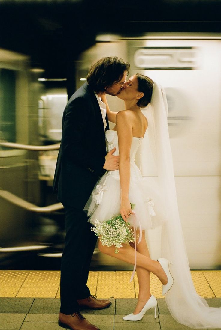 a bride and groom kissing in front of a subway train at their wedding day,