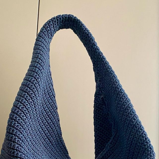 a blue crocheted bag hanging from a hook on a wall in front of a white wall