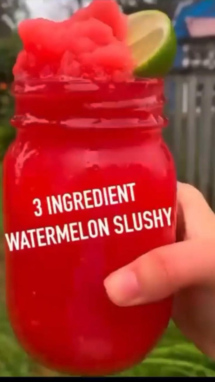 someone is holding a red mason jar with watermelon slushy inside it