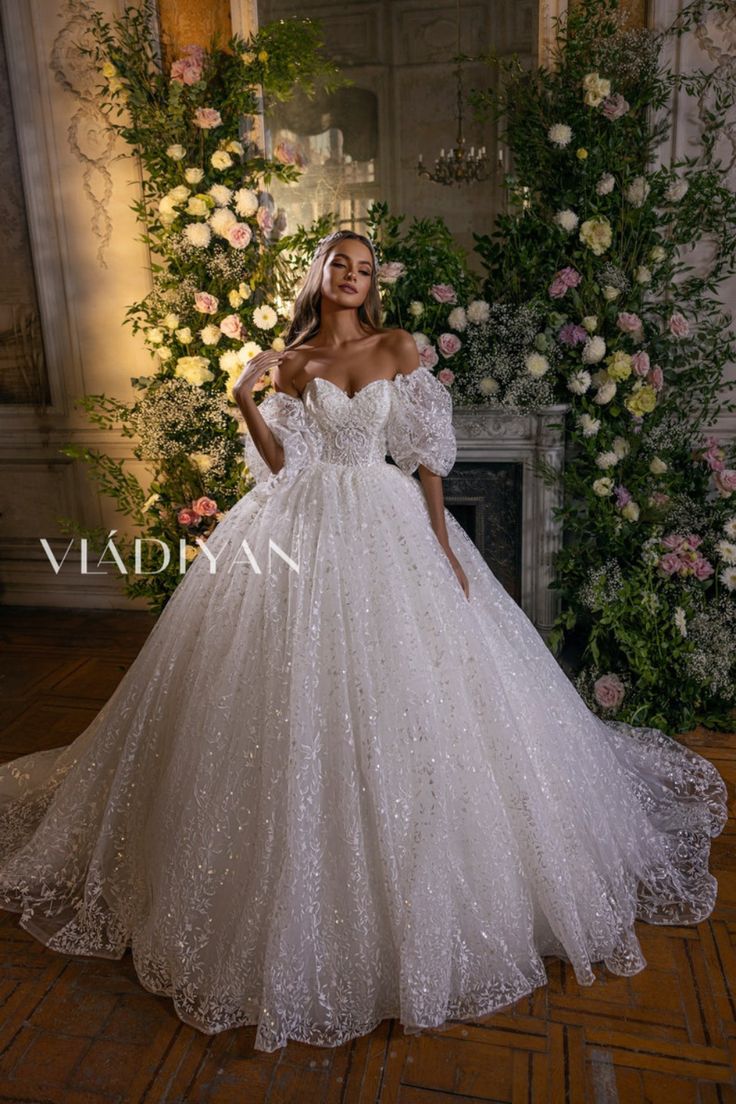 a woman in a white wedding dress standing next to a floral wall with flowers on it