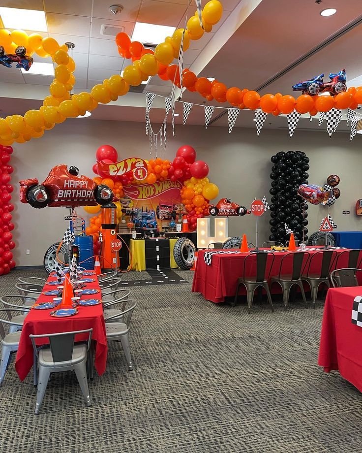 a room filled with lots of balloons and tables covered in red tablecloths, race cars