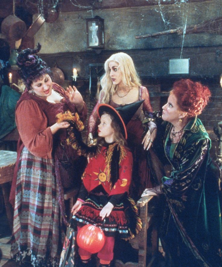 three women dressed up as witches and one is holding a pumpkin in her hand while the other looks on