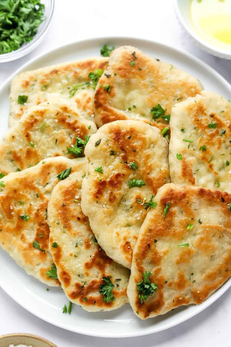 several flat breads on a white plate next to bowls of sauce and parsley