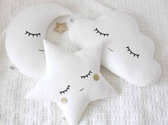 two white pillows with stars and eyelashes on them, one is shaped like a crescent