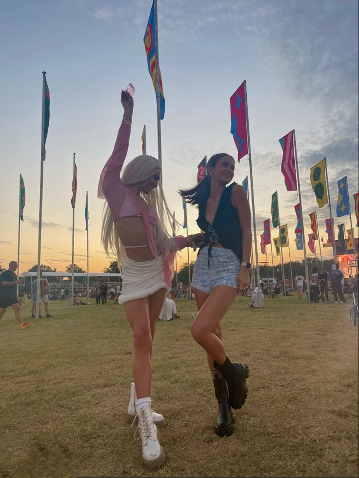 two young women dancing in the grass with flags flying behind them at an outdoor music festival