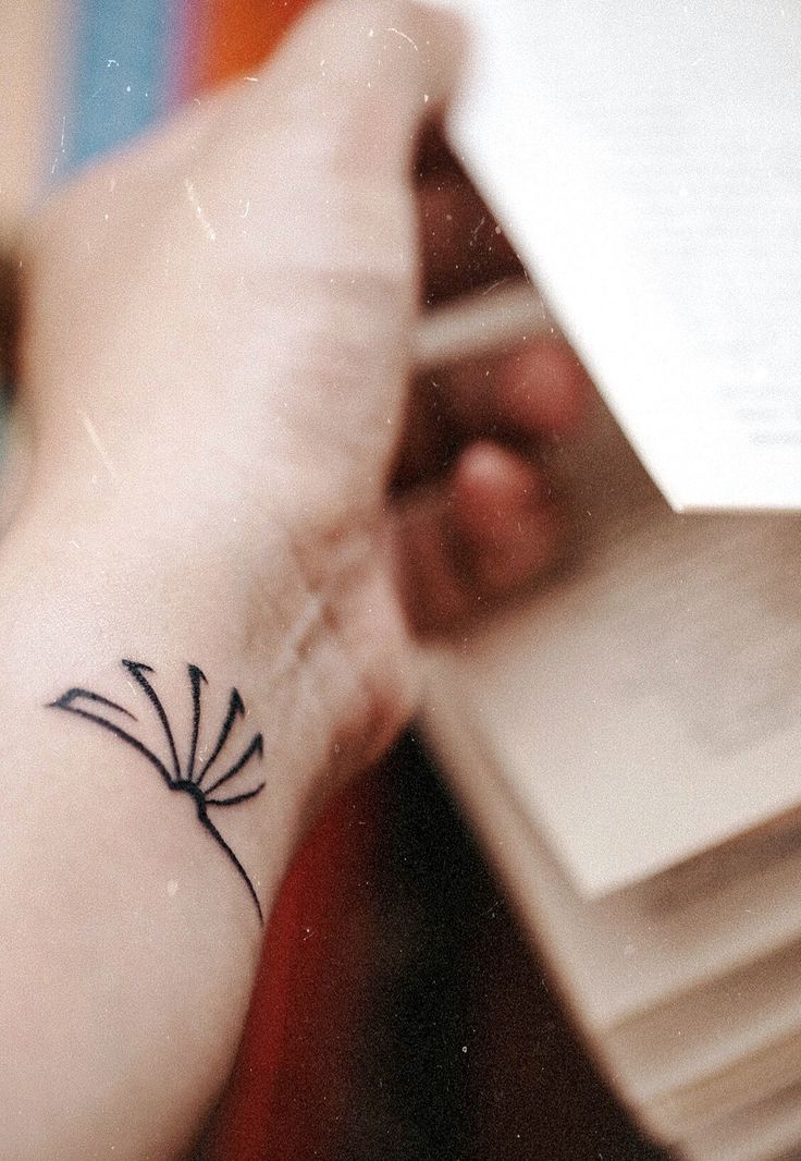 a woman's arm with a small tattoo on her left wrist and an open book in the other hand