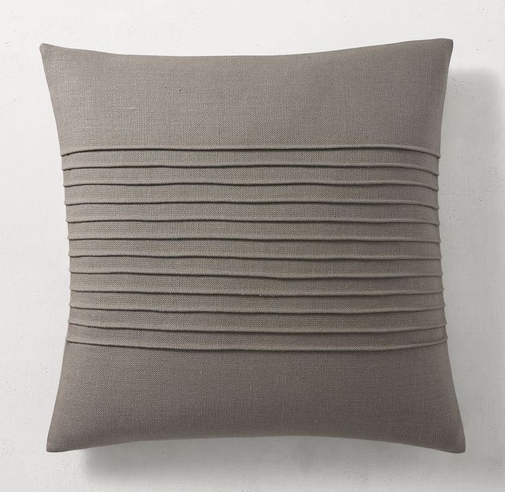 a gray pillow with pleated lines on the front and back, against a white wall