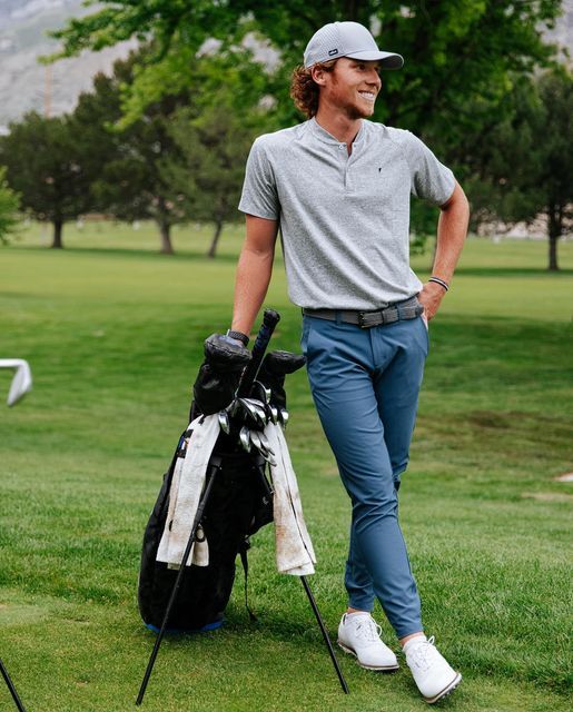 a man standing on top of a lush green field holding a golf club and bag