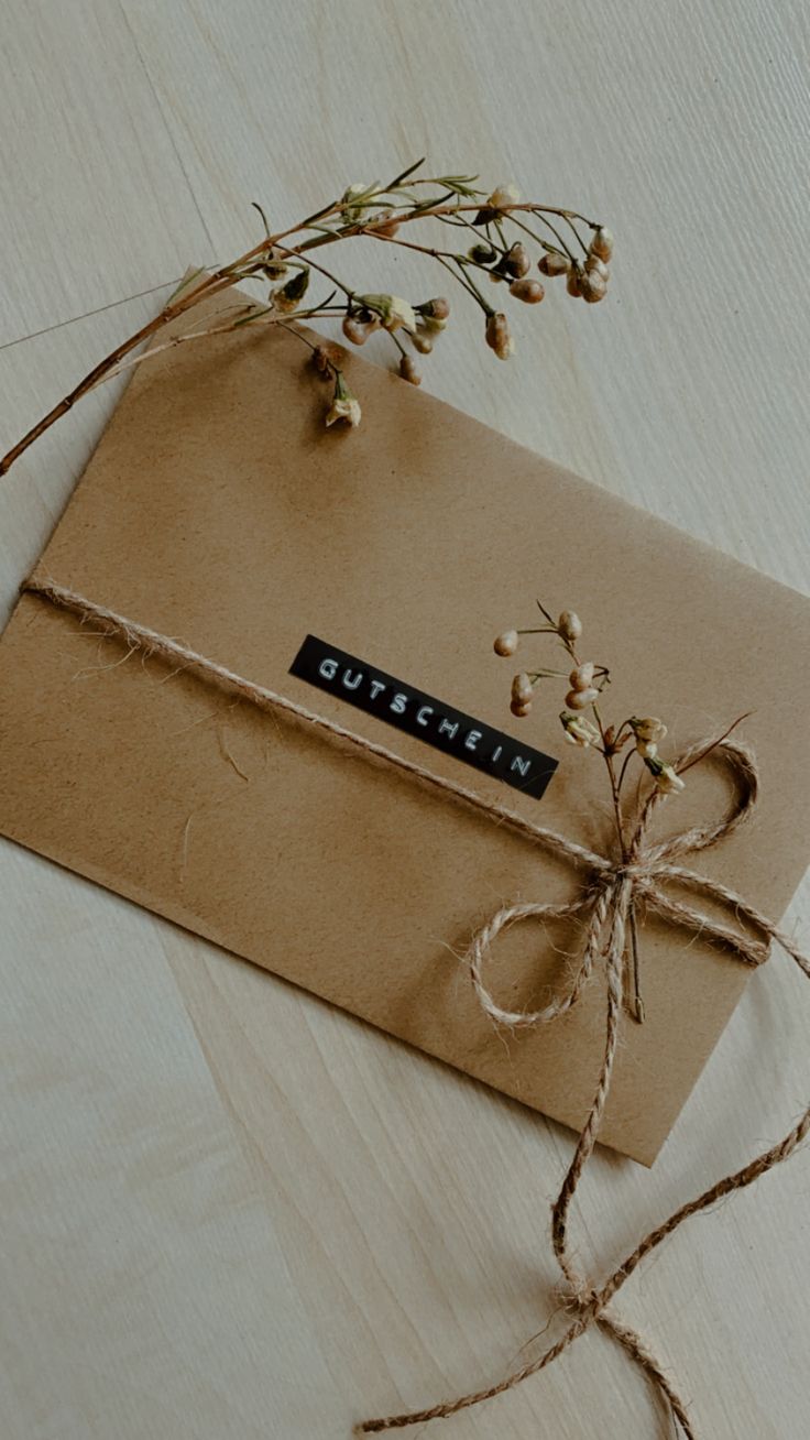 a brown envelope tied with twine on top of a wooden table next to dried flowers