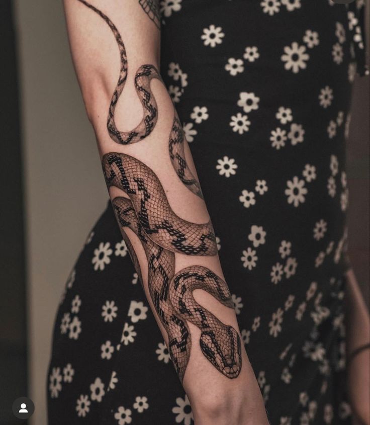 a woman's arm with a snake tattoo on it and flowers around the arm