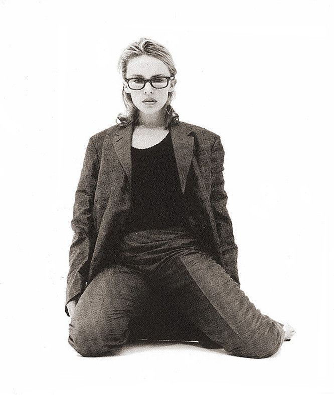 a black and white photo of a woman in glasses sitting on the floor with her legs crossed