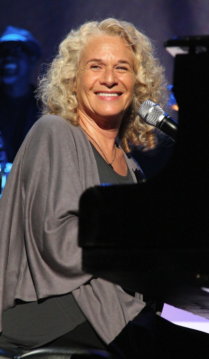 a smiling woman sitting at a piano in front of a microphone