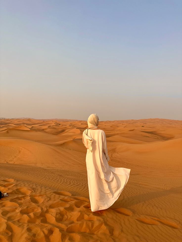 a person standing in the middle of a desert with sand dunes and blue sky behind them