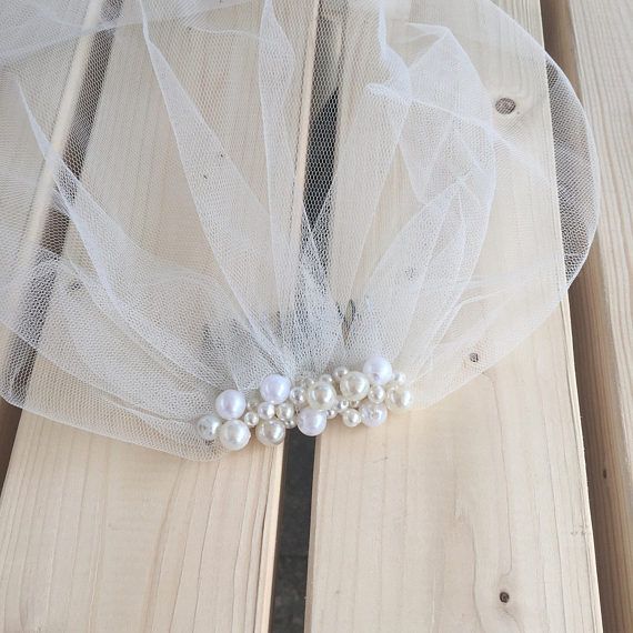 a white veil with pearls on it sitting on top of a wooden table next to a pair of scissors