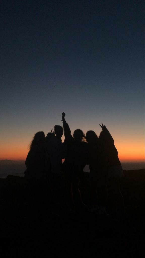 a group of people standing on top of a mountain at sunset with their arms in the air