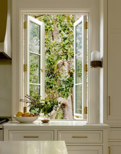 an open window in a white kitchen with trees and plants on the wall behind it