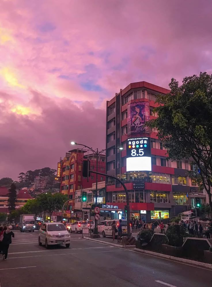 a city street filled with traffic and tall buildings under a cloudy sky at dusk,