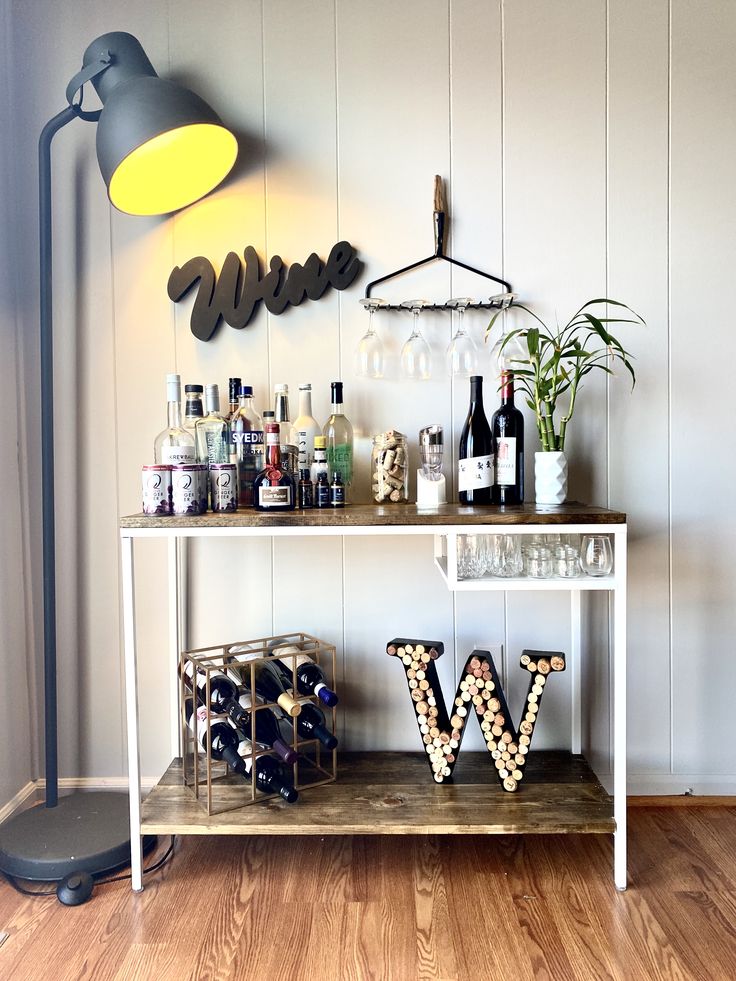 a bar cart with wine bottles and glasses on it in front of a wall mounted sign