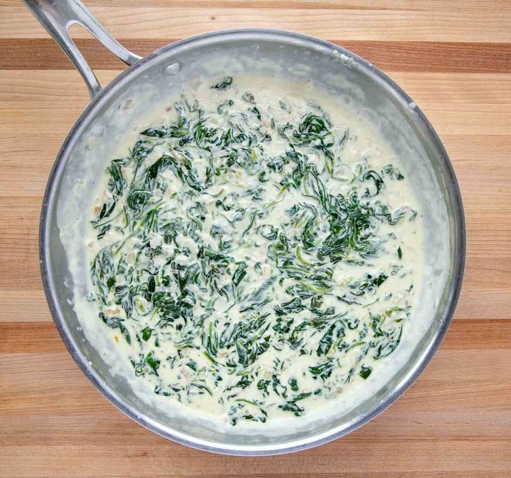 a pan filled with spinach and cheese on top of a wooden table