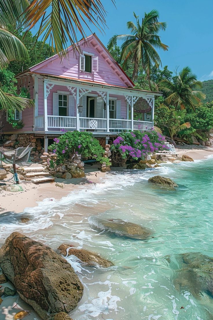 a pink house sitting on top of a sandy beach next to the ocean and palm trees