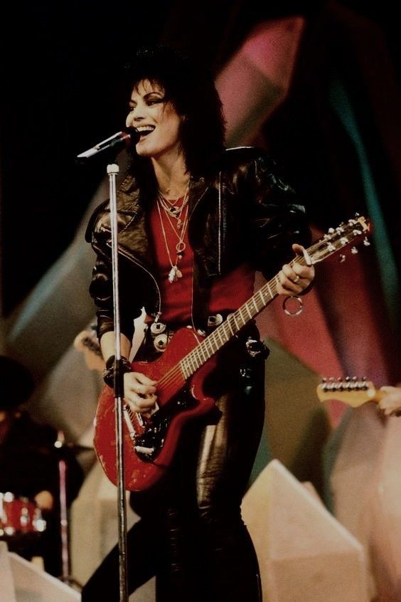 an image of a woman singing into a microphone and playing the guitar in front of her