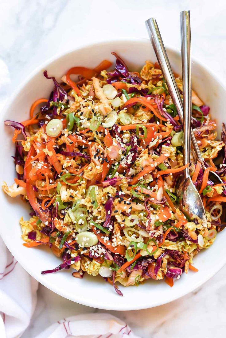 a white bowl filled with coleslaw slaw and two silver serving spoons