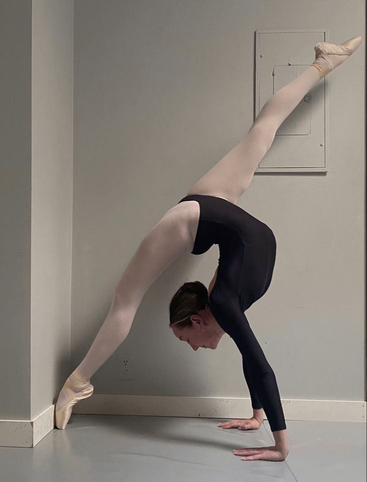 a woman doing a handstand on the floor in front of a white wall