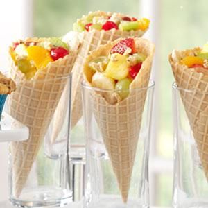 three cones filled with fruit and ice cream on top of a table next to glasses