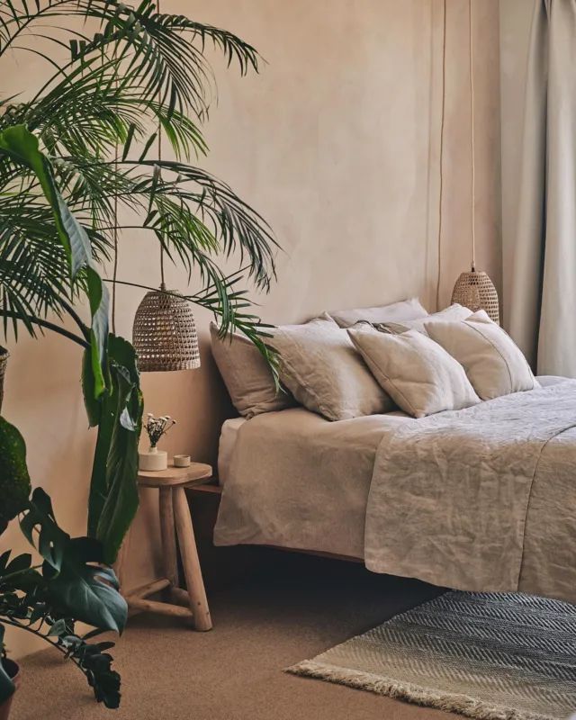 a bed sitting next to a tall plant in a bedroom under a light colored wall