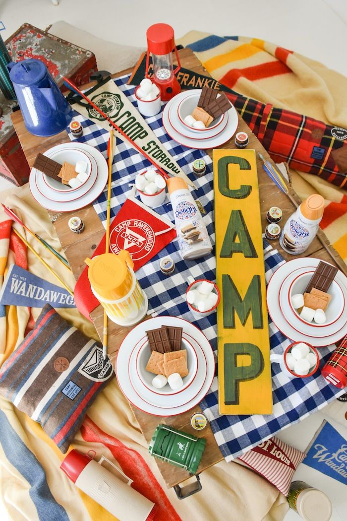 a camp sign is surrounded by food and camping utensils on a picnic blanket