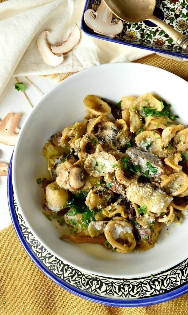 a white bowl filled with pasta and mushrooms on top of a yellow table cloth next to silverware