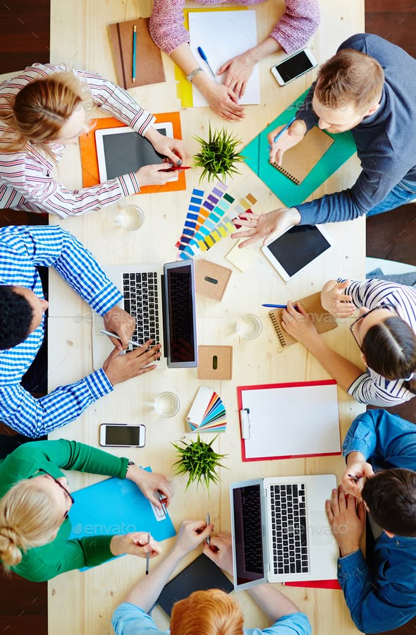 four people sitting at a table with laptops and notebooks in front of them