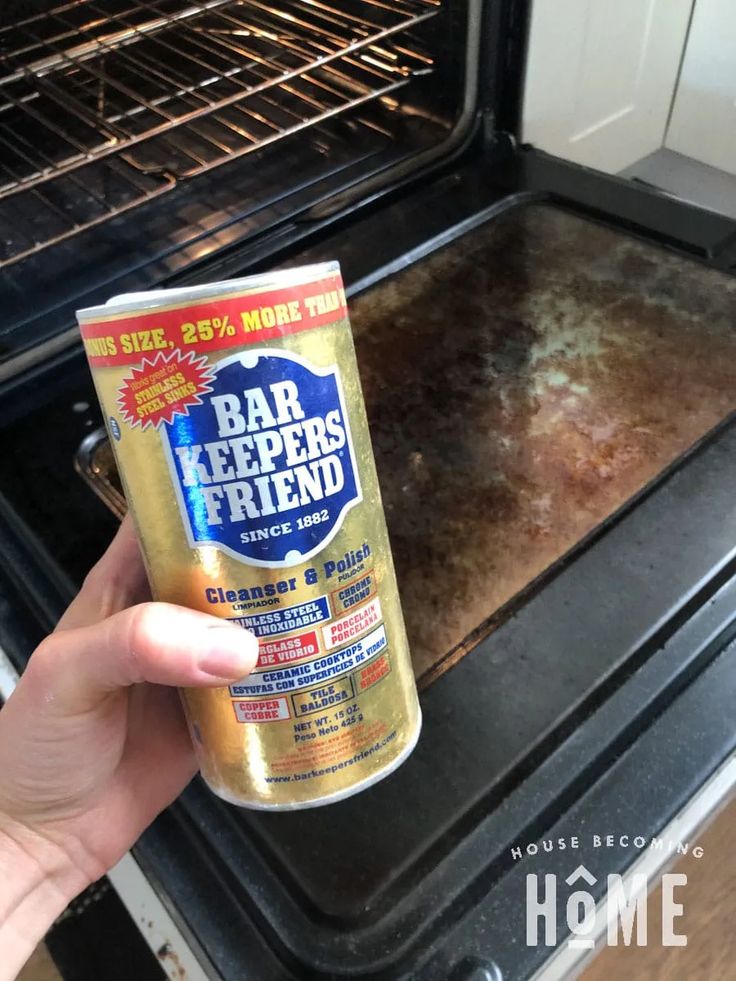 someone holding up a can of bar keepers friend in front of an oven with the door open