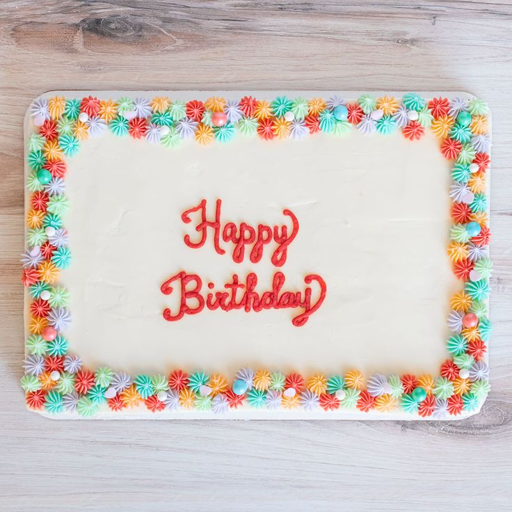 a birthday cake with white frosting and colorful flowers on the side that says happy birthday