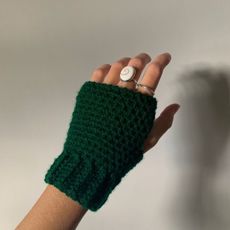 a woman's hand wearing a green crocheted fingerless mitt with a button on it