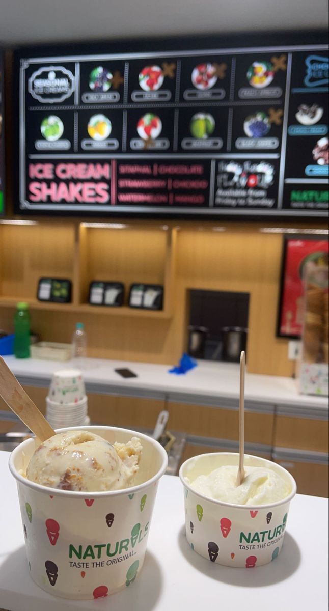 two ice cream cups sitting on top of a counter next to a tv screen in a restaurant