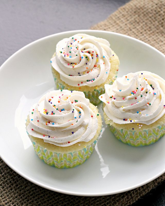 three cupcakes with white frosting and sprinkles on a plate