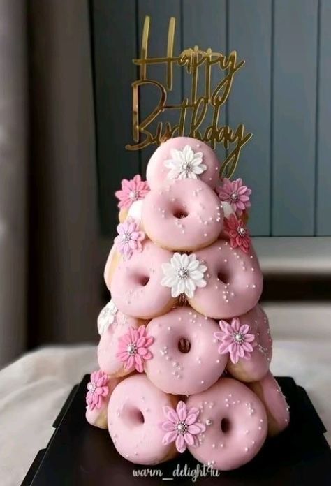 a birthday cake made out of donuts with pink frosting and flowers on top