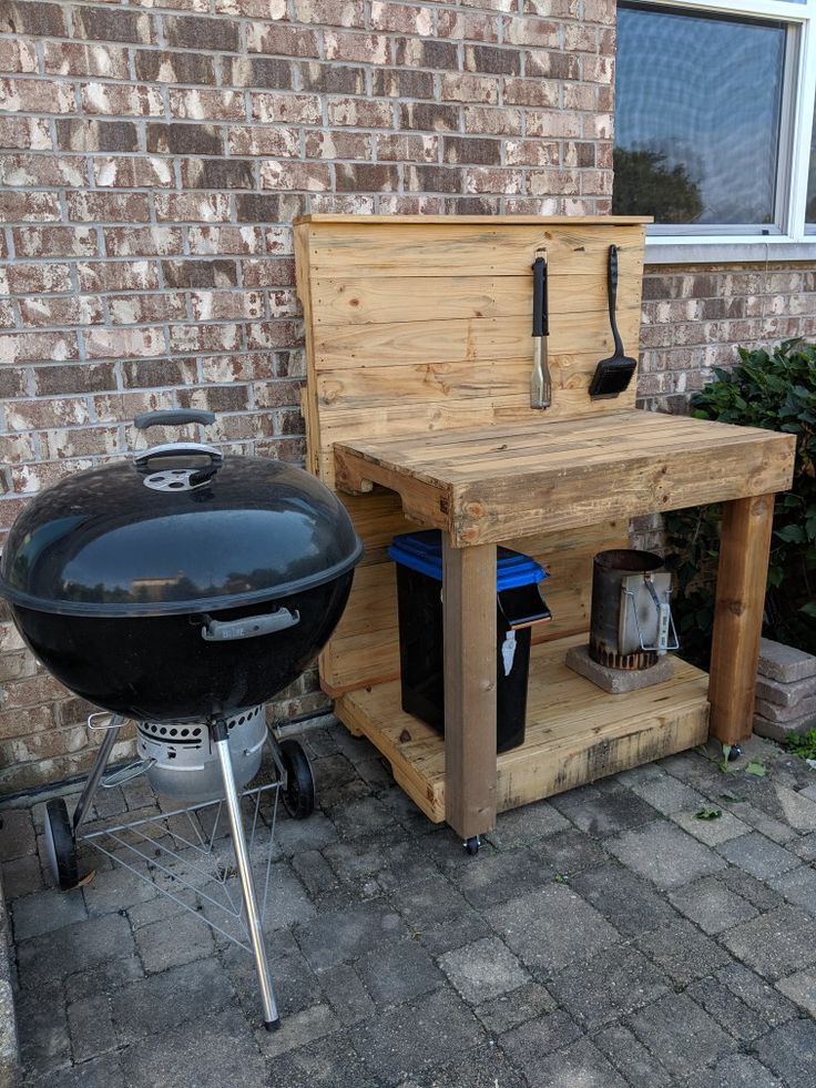 an outdoor bbq with grill and barbecue tools on the side of it in front of a brick building