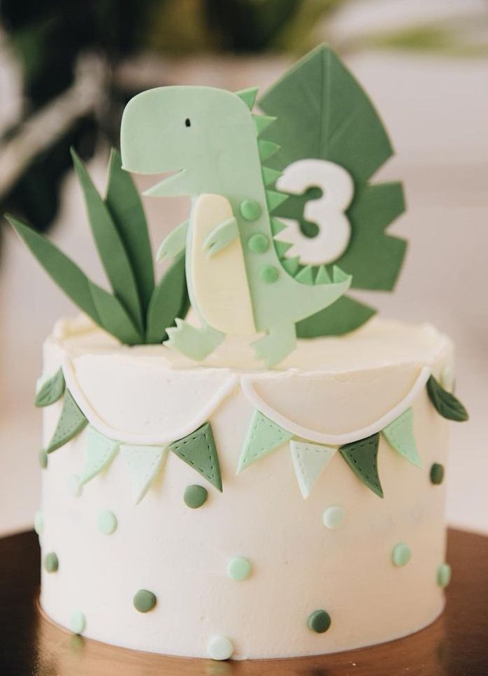 a birthday cake decorated with green and white decorations on a wooden table in front of a plant