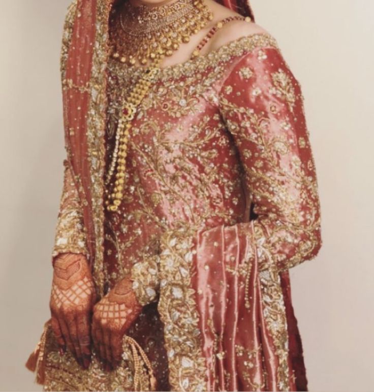 a woman in a red and gold bridal gown with jewelry on her head, standing next to a white wall